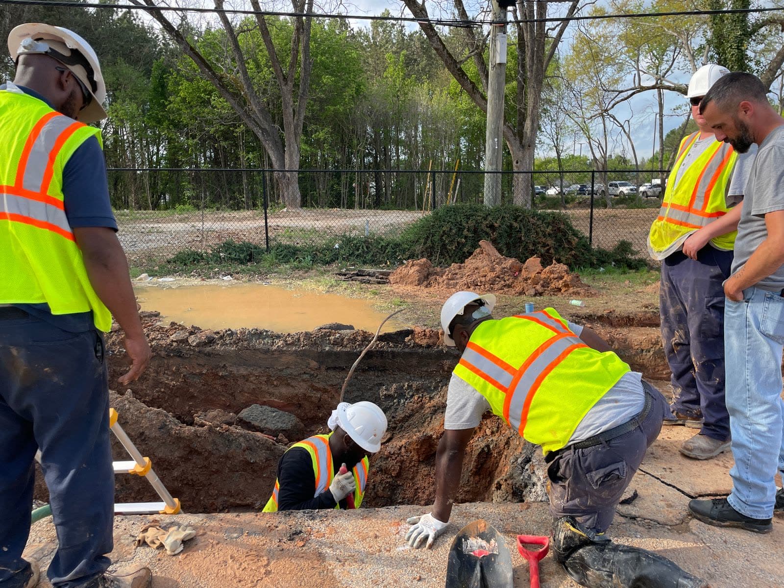 A municipal crew in high-visibility vests working at an open excavation around an underground utility line